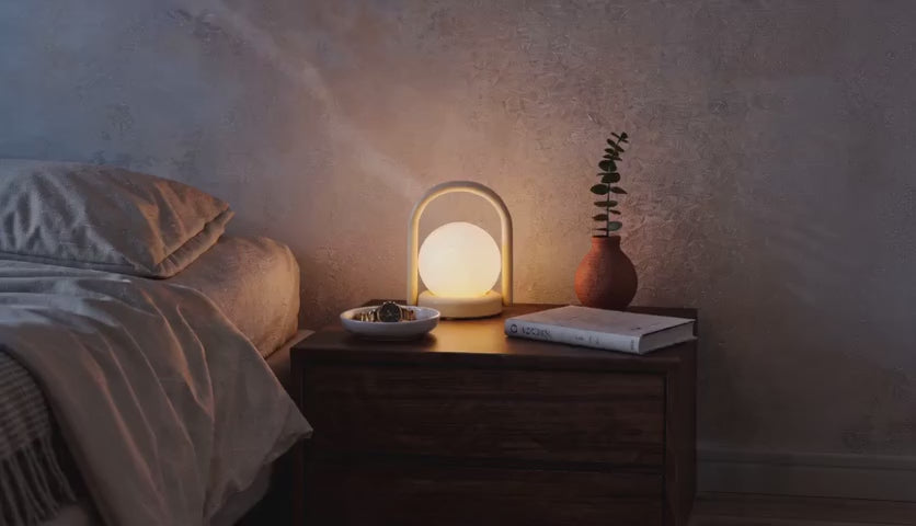 Charger la vidéo : Cinematic video of a cordless LED globe lantern lamp glowing softly on a wooden bedside table in a dim bedroom.