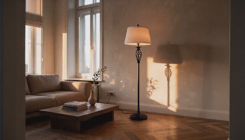 Charger la vidéo : Cinematic video of a black metal floor lamp with twisted cage column and white drum shade casting warm shadows in a sunlit living room.